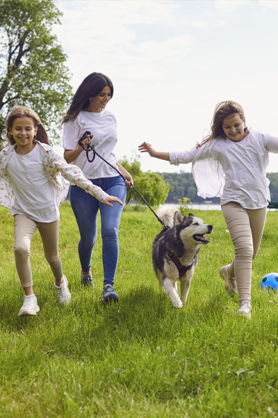Image of mother and children running at park with their dog.