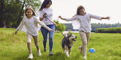 Image of mother and children running at park with their dog.