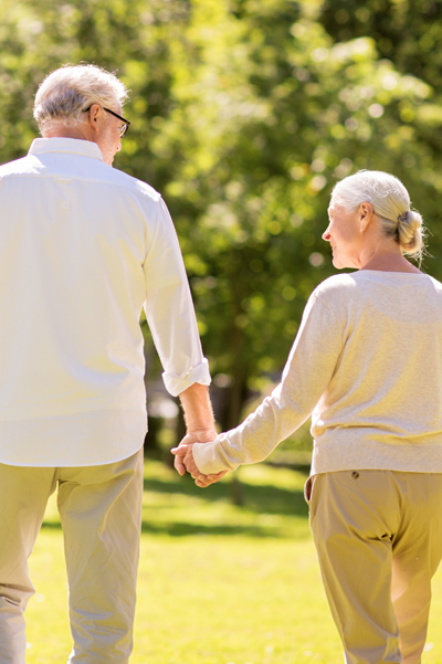 Image of senior couple walking in park holding hands.
