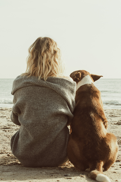 Image of woman sitting with dog on beach.
